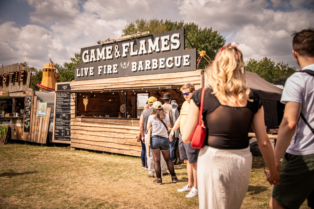 Game and Flames Live Fire Barbecue stand at an outdoor festival with crowds
